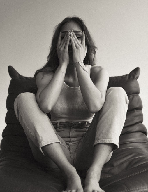 Kobieta siedząca boso na fotelu z rękami na twarzy